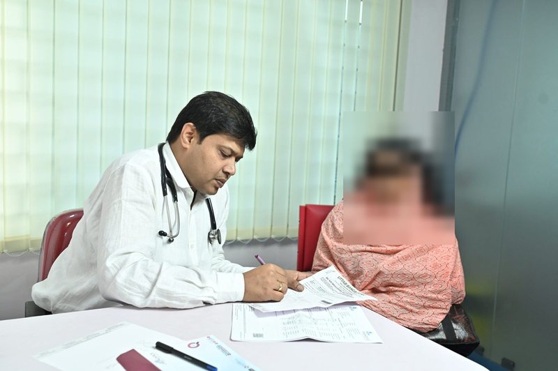 Dr Soumya Ghosh writing a prescription during a consultation at Uttarbanga Clinic, Cooch Behar. The patient's face has been obscured to protect her identity